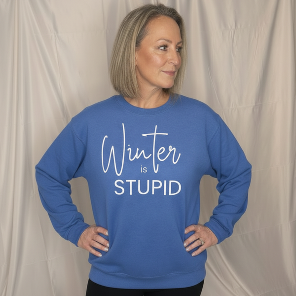A woman in an indigo Blue "Winter is Stupid "sweatshirt standing with a white backdrop.