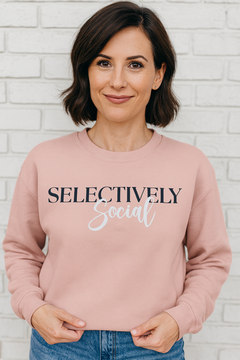 Woman wearing a pink sweatshirt with 'SELECTIVELY Social' text against a white brick wall.