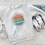 Ash gray vintage birthday sweatshirt laid flat, showing the retro sunset birth year design.