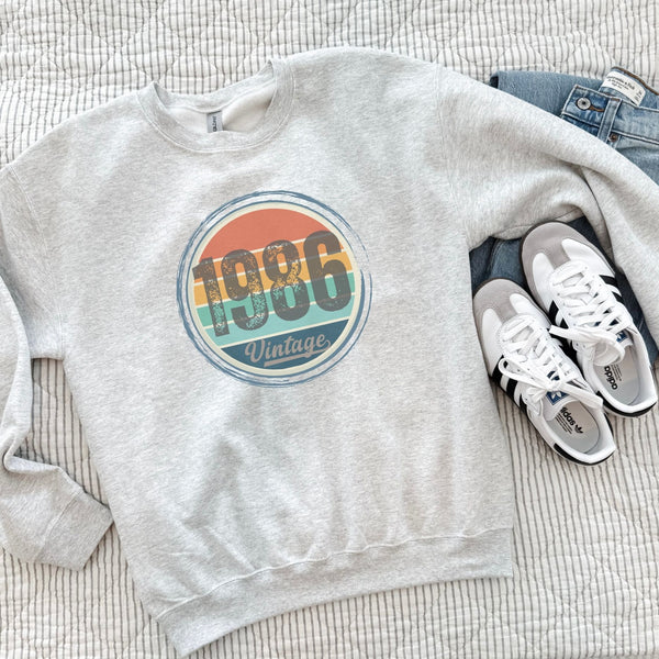 Ash gray vintage birthday sweatshirt laid flat, showing the retro sunset birth year design.