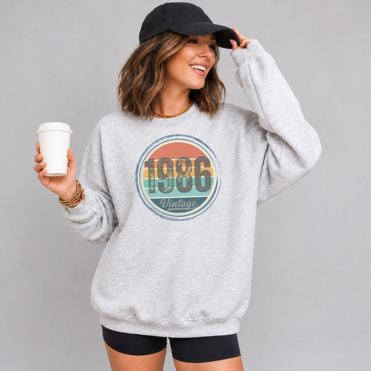 Woman wearing an ash gray vintage birthday sweatshirt with a retro sunset birth year badge.