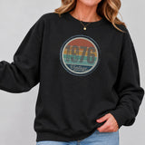 Close-up of the retro sunset birth year badge on a black vintage birthday sweatshirt.