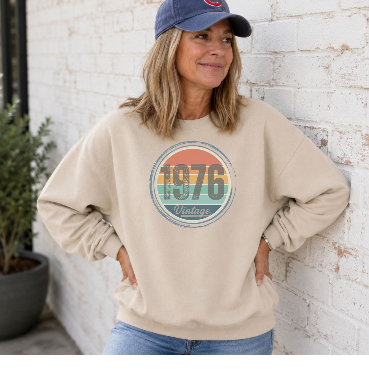 Woman wearing a sand vintage birthday sweatshirt with a retro 1976 birth year badge.